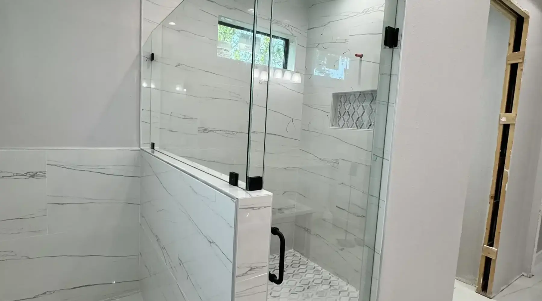 Semi-frameless glass shower enclosure with knee wall and matte black hardware installed in white marble bathroom — Glass Designer LLC FL