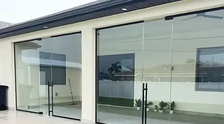 Side-by-side custom frameless glass shower enclosures with matte black hardware and marble tile — Glass Designer LLC Naples FL